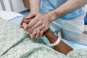Close-up of unrecognizable man holding woman's hand at her bedside in hospital
