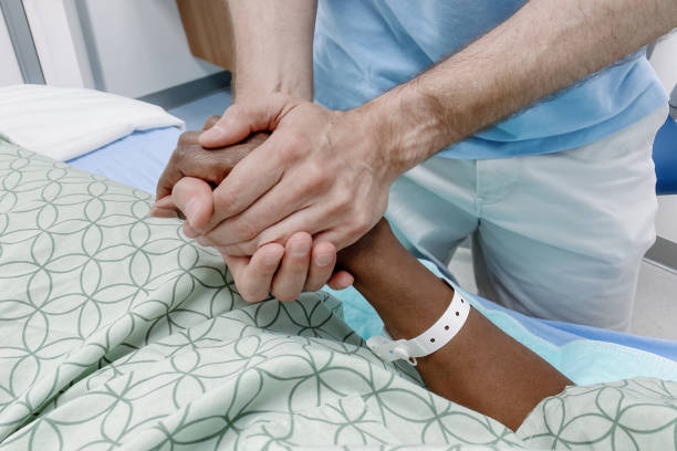 Close-up of unrecognizable man holding woman's hand at her bedside in hospital